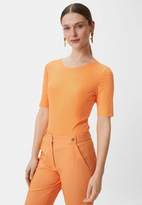Pomarańczowa bluzka z krótkim rękawem i prążkowanym wzorem, z okrągłym dekoltem, zestawiona z dopasowanymi pomarańczowymi spodniami z dyskretnym logo na pasku.