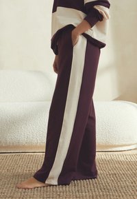 Bordo trenirka s kremnimi črtami na straneh, z raztegljivo obliko in stranskim žepom. Iz mehke tkanine, z gladko teksturo.