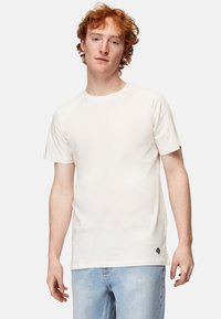 Hvid bomulds t-shirt med klassisk rund hals, korte ærmer og en lille sort logo-accent på sømmen. Glat tekstur, afslappet pasform.