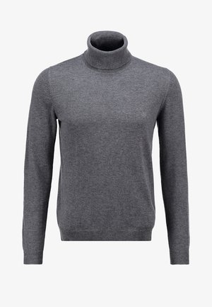 Uomo che cammina indossando una giacca nera, un maglione a collo alto grigio, pantaloni neri e stivali marroni con lacci su uno sfondo neutro.
