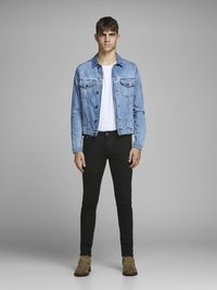 Chaqueta de mezclilla azul claro con dos bolsillos en el pecho, camiseta blanca, jeans ajustados negros y botas de ante marrones hasta el tobillo. Atuendo simple y casual.