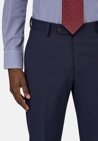 Marineblauwe broek van gestructureerde stof, met een slim fit, knoopsluiting, en een gestreept overhemd en een stippenstrik zichtbaar.