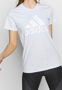 Camiseta de algodón azul claro con un gran logo blanco de Adidas en el pecho. Mangas cortas y un diseño clásico de cuello redondo.