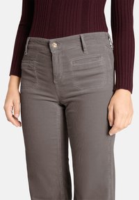 Grijze corduroy broek met een gestructureerde afwerking, voorzien van steekzakken aan de voorkant en een gouden knoop. Draagt bijpassend een geribbelde bordeauxrode top.