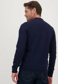 Marineblauwe gebreide trui met lange mouwen en een ronde halslijn, met een gestructureerde afwerking en ribgebreide manchetten, gecombineerd met donkere spijkerbroeken.