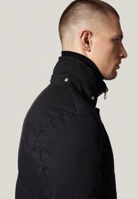 Czarna pikowana kurtka z wysokim kołnierzem, zapięciem na zamek błyskawiczny oraz zatrzaskami. Gładka tekstura z kontrastującym prążkowanym wykończeniem kołnierza.