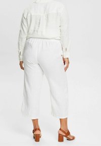 Vit lin skjorta med sprund i ärmarna, i kombination med lösa vita byxor. Bruna sandaletter med blockklackar fulländar outfiten.