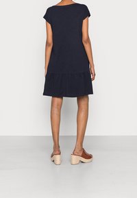 Lautan biru, gaun bertingkat lengan pendek dengan potongan longgar; terbuat dari kain ringan. Dipakai dengan sandal platform anyaman.