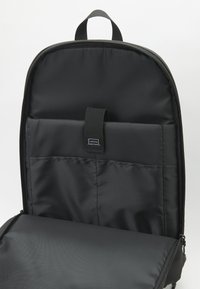 Čierny batoh so hladkým nylonovým povrchom, ktorý má zipsovú priehradku a polstrovaný obal na laptop vo vnútri. Minimalistický dizajn.