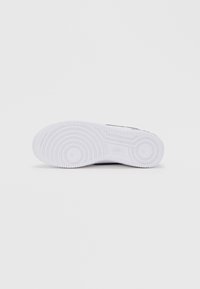 Λευκή σόλα αθλητικού παπουτσιού με υφή, που διαθέτει κυκλικά μοτίβα και αυλακώσεις για πρόσφυση, κατασκευασμένη από καουτσούκ με λεία επιφάνεια.