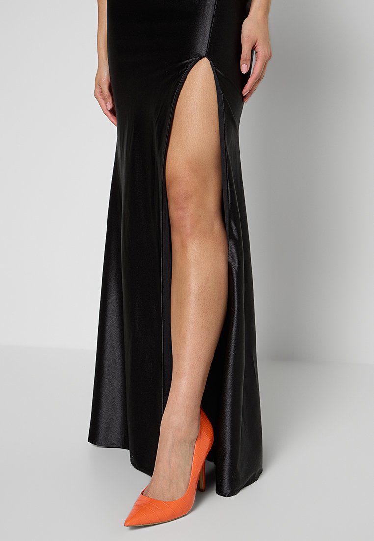 Maxi dress in satin nera con uno spacco alto fino alla coscia, abbinato a tacchi a punta in pelle coccodrillo arancione brillante. Tessuto liscio e design elegante.