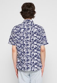 Camicia a maniche corte in tessuto blu navy con motivo floreale e fogliare bianco. Presenta un colletto a punta e un taglio dritto.