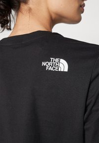 Must tume mustvalgest puuvillast T-särk, millel on valge "The North Face" logo ülaseljal, lühikesed varrukad ja klassikaline ümmargune kaelus.