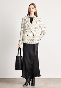 Διπλό σακάκι σε λευκό και μαύρο κλωστοϋφαντουργικό υλικό, συνδυασμένο με μία μαύρη σατέν φούστα με κρόσσια από δαντέλα και μαύρες γόβες.