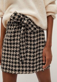 Gonna a fantasia houndstooth nera e crema con un fiocco in vita, caratterizzata da un tessuto testurizzato e un design corto e aderente.