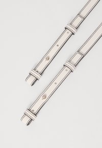Sangles en cuir synthétique blanc avec des coutures noires, dotées de fermoirs en métal et de plusieurs trous ajustables pour personnaliser la longueur.