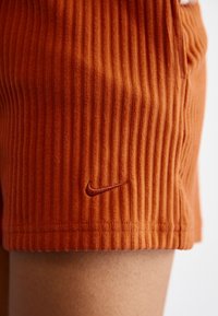 Orange ribbade shorts i mjuk tyg. Har en liten broderad Nike-logga i en matchande nyans nära fållen.