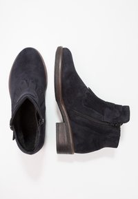 Mörkblå mocka ankelboots med låg klack, utrustade med en sidodragkedja, dekorativa detaljer och en strukturerad sula för bra grepp.