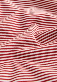 Rdeče-belo prozorna bombažna tkanina z mehkim, teksturiranim videzom, ki prikazuje gladke valove in izrazite izmenične črte.