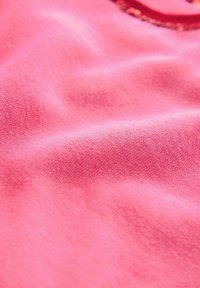 Rožinė medvilnė, turinti minkštą, šiek tiek tekstūruotą paviršių ir silpną įstrižinę audimo raštą, rodanti švelnius raukšles ir klostes.