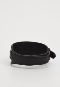 Bracciale in pelle nera con una texture liscia, caratterizzato da un design avvolto e un piccolo anello accento per la chiusura. Logo inciso all'interno.