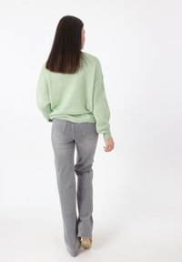 Langärmliger, hellgrüner Strickpullover, kombiniert mit enganliegenden, hellgrauen Jeans. Der Pullover hat einen lockeren Schnitt und gerippte Bündchen.