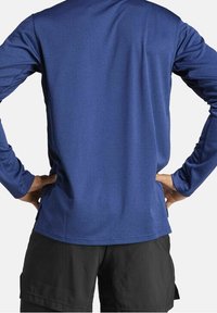 Dlouhý rukáv atletického trička v námořnické modři, vyrobeného z vlhkost odvádějící tkaniny, má kulatý výstřih a zakřivený lem, doplněného o černé šortky.