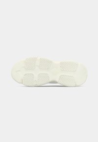 Suela de zapatilla blanca con almohadillas de goma segmentadas que presentan un patrón de chevron sobre un fondo gris claro.