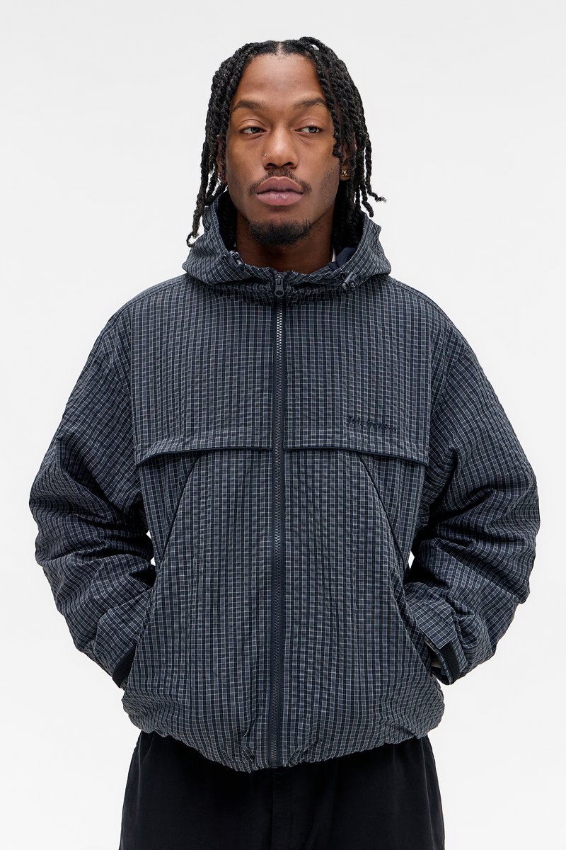 Casaco puffer em cinza escuro com um padrão em grelha, capuz, fecho de zipper e bolso frontal. Superfície texturizada com um leve brilho.