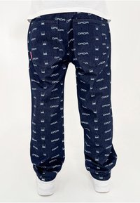 Joggings en denim foncé avec un motif répétitif de couronnes blanches et du logo "DADA". Coudes élastiques et poches au dos.