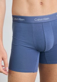Kék pamutkeverék boxeralsó, testhez simuló fazonnal és rugalmas derékpánttal, amelyen a Calvin Klein fehér logója található.