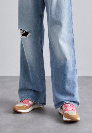 Sneakers med en beige og lyserød farveskema, med en struktureret overdel, snørebånd og en brun sål. Båret med lyseblå slidte wide-leg jeans.