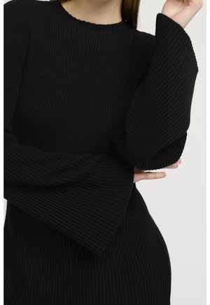 Robe noire côtelée avec un col rond et des manches évasées texturées. Le tissu a une finition douce en tricot, mettant en valeur une silhouette ajustée.