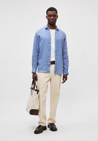 Μπλε και λευκή ριγέ πουκάμισο μακρύς-μανίκι, κρέμα παντελόνι, σκούρες καφέ παπούτσια, και μπεζ τσάντα tote με καφέ λεπτομέρειες. Χαλαρή εμφάνιση.