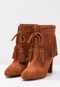 Brązowe zamszowe botki za kostkę z frędzlami i związaniami, z wysmuklonym noskiem i średniej wysokości drewnianym obcasem.