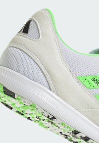 Szare sportowe buty z zielonymi akcentami, wykonane z zamszu i siateczki, z zaokrąglonym obcasem, wzorzystą gumową podeszwą oraz widocznym logo na boku.