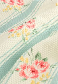 Tkanina z reliefom v kremno modrih črtah, z rožnatimi in rumenimi cvetličnimi vzorci. Mehka, valovita površina z izrazitimi teksturami.