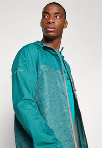 Teal lichtgewicht hooded jack met een textuurdesign, contrasterende oranje rits en meshvoering. Glad materiaal met functionele accenten.
