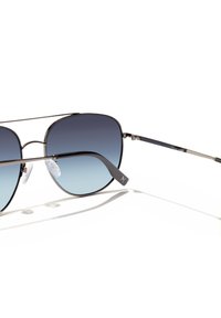 Ochelari de soare aviator cu rame metalice, lentile de culoare albastră cu efect de degradare și brațe subțiri negre, așezate pe o suprafață albă.
