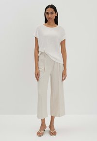Weißes, geripptes Kurzarmoberteil kombiniert mit hellbeigen, weit geschnittenen Hosen. Das Model trägt flache Sandalen. Einfaches und minimalistisches Design.