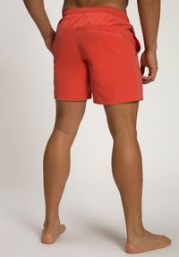 Heren zwemshorts in koraalkleur met een elastische tailleband, zijzakken en een achterzak. Een gladde textuur en een lengte tot boven de knie.