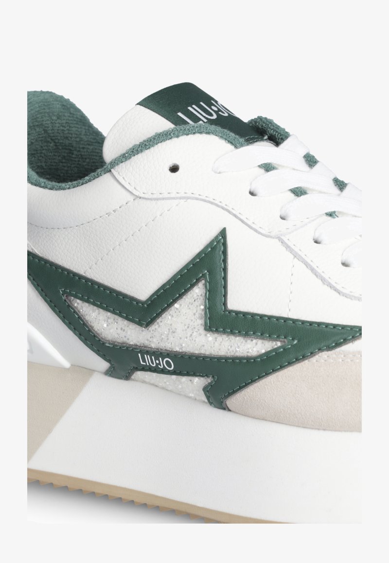 Witte sneaker met groen ster ontwerp, groene binnenvoering, witte veters en beige suède neuskap detail.