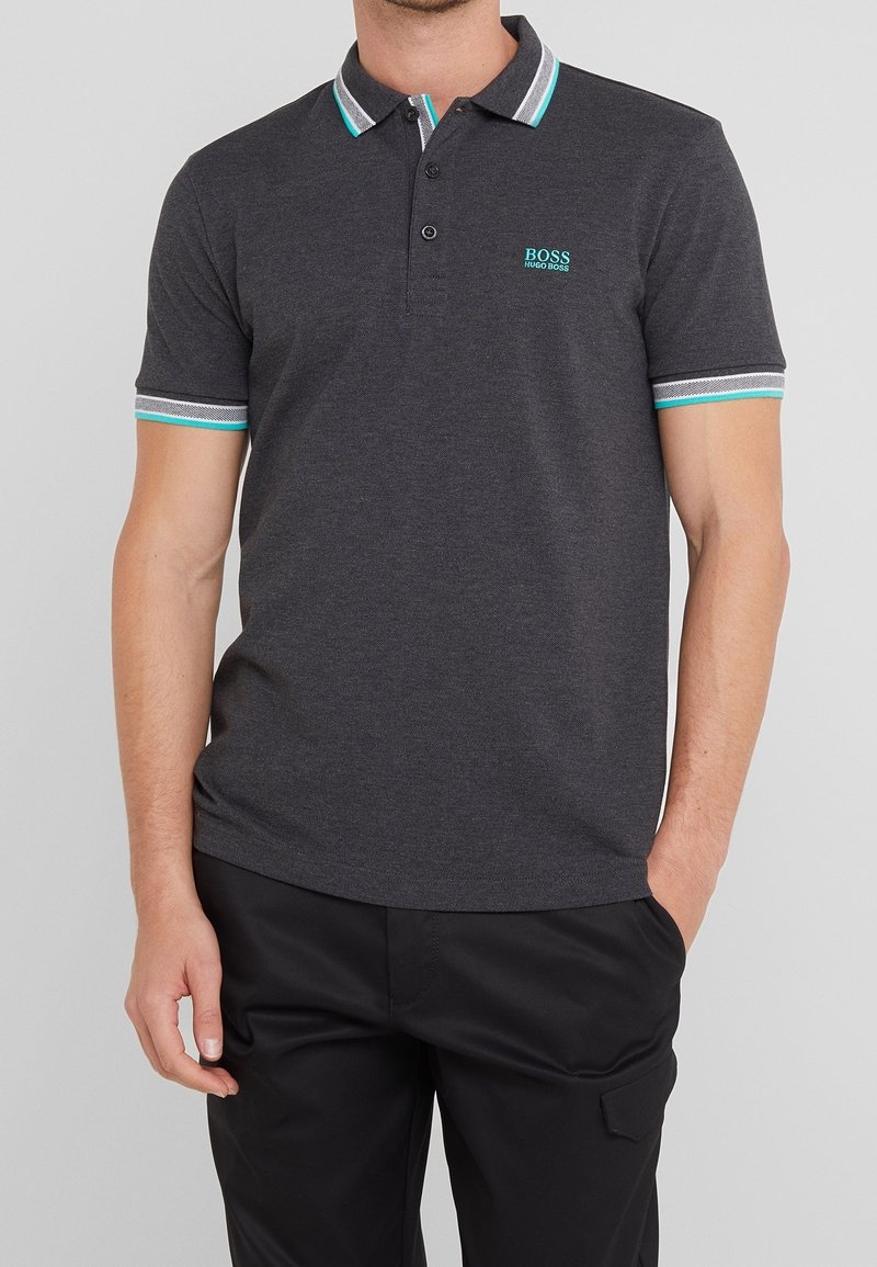 Man bär en mörkgrå polo med krage och ärmvrang av turkos och vit rand, samt "BOSS HUGO BOSS" logga på bröstet.
