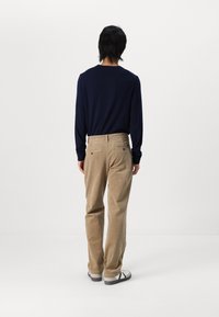 Marineblauw shirt met lange mouwen gecombineerd met lichtbruine corduroy broek. De broek heeft een rechte pasvorm en achterzakken met knoopsluitingen.
