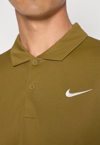 Oliven grønn polo skjorte laget av glatt stoff, med en to-knapp placket, klassisk krage, og en hvit Nike-logo på venstre bryst.