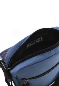 Bolsa de tela azul con cierre de cremallera. Presenta un exterior texturizado y un forro negro. La marca es visible en el interior en la etiqueta.