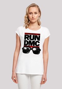 Weißes Baumwoll-T-Shirt mit einem auffälligen schwarzen und roten Grafikdruck, der "RUN DMC" mit Sonnenbrille zeigt. Kurze Ärmel und lockere Passform.