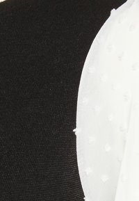 Tessuto nero aderente con una superficie texturizzata a sinistra, accompagnato da tessuto bianco trasparente a destra, caratterizzato da pois in rilievo.