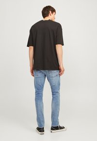 Camiseta negra de manga corta con un corte holgado, combinada con jeans ajustados de color azul claro y zapatillas negras con cordones blancos.