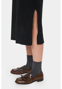 Černá pletená sukně se bočními rozparky, v kombinaci s hnědými koženými mokasíny s franjemi a vroubkovanými šedými ponožkami. Texturovaný a precizně ušitý design.